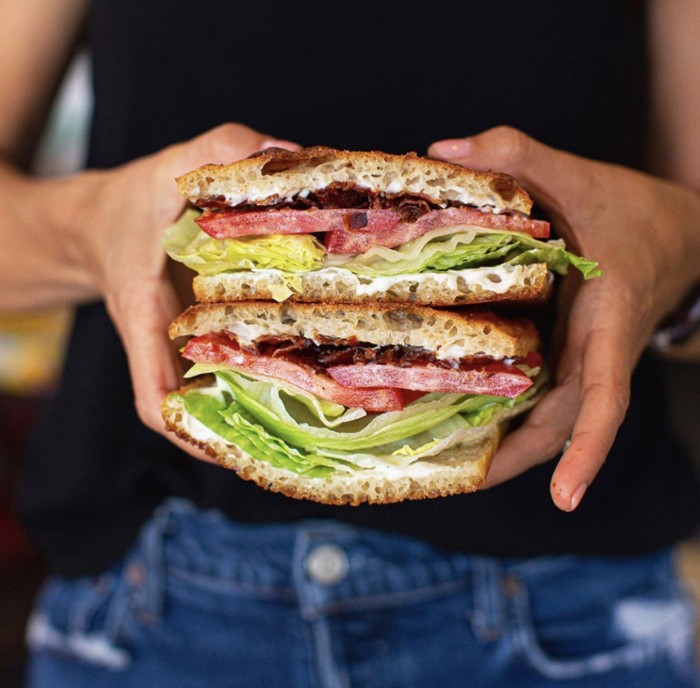 BLT stacked and held in two hands in front of a black shirt