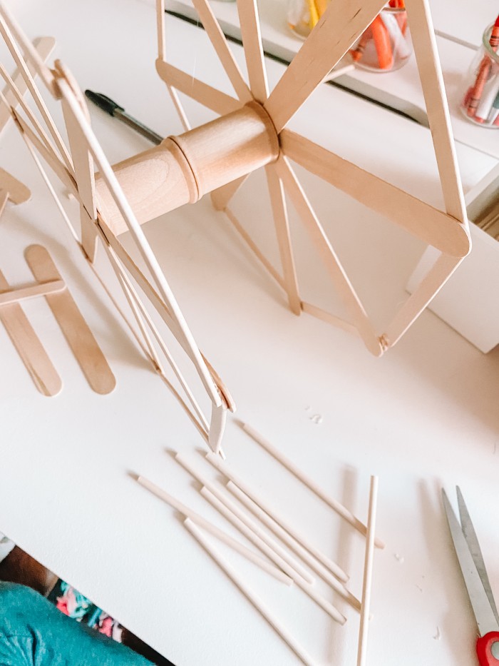 Popsicle sticks glued to wooden spools to form a Ferris wheel, sitting on a white table