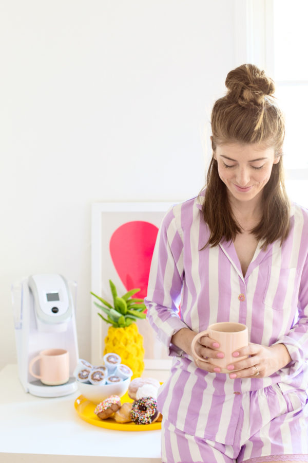 A woman holding a cup of coffee on a table, wearing purple and white stripped shirt 