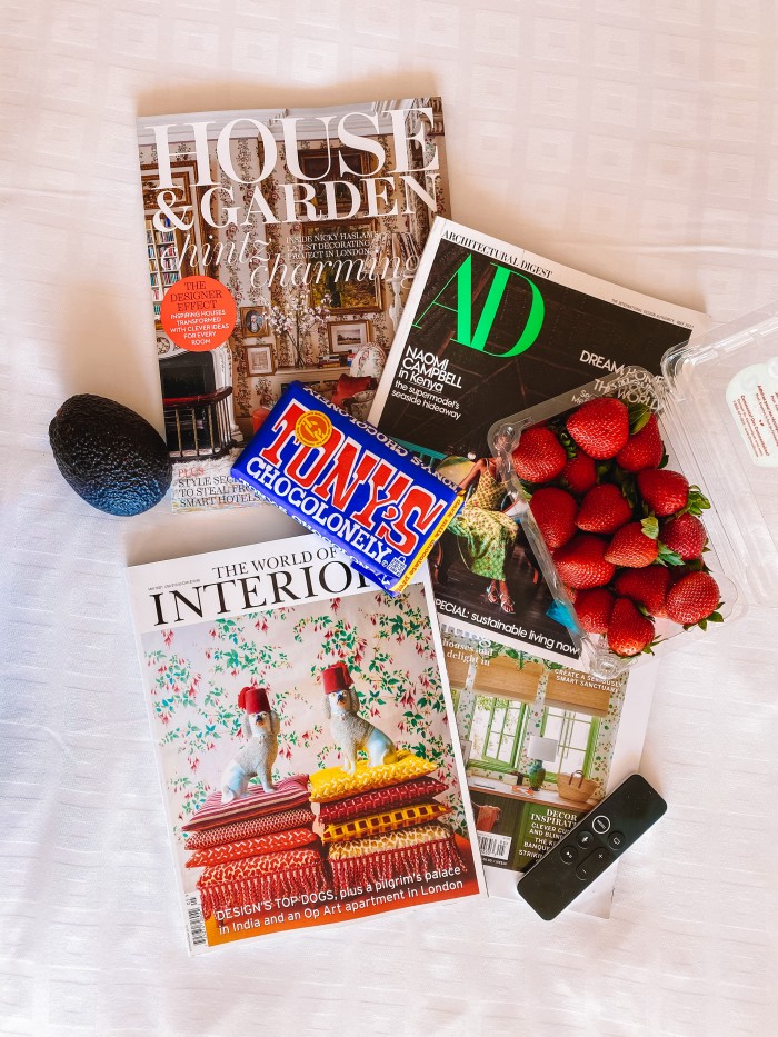 Shelter magazines, strawberries, chocolate bar and avocado laying on a bed