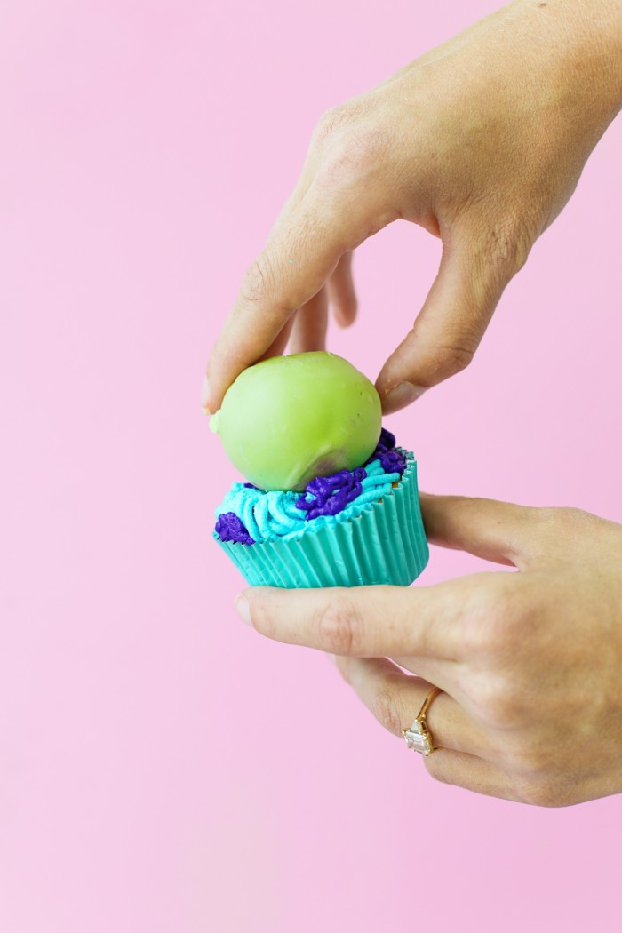 Green cake ball onto of blue and purple frosted Monster cupcake