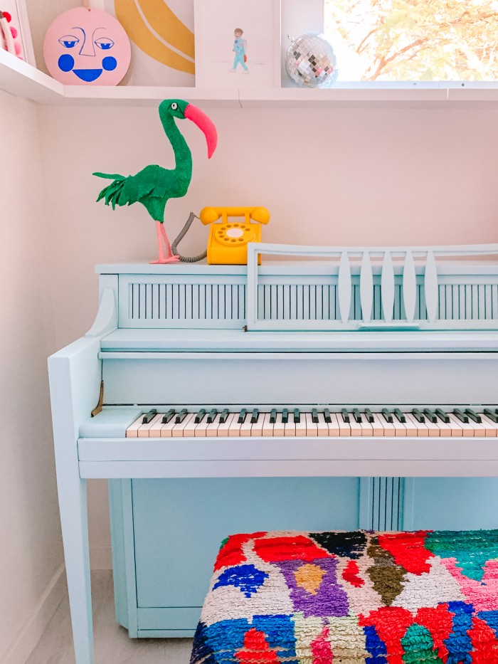 Blue piano in a corner with colorful textile bench and a yellow phone on top