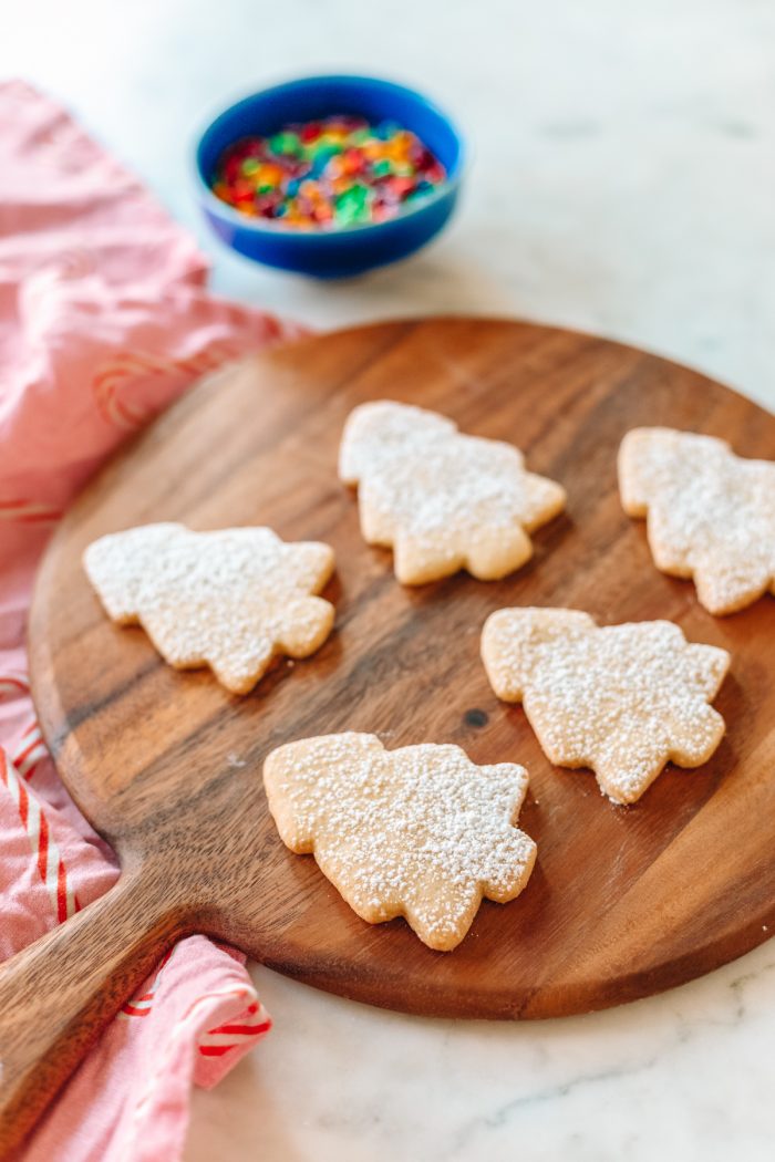 Sugar cookies in the shape of trees on a wooden cutting board. 