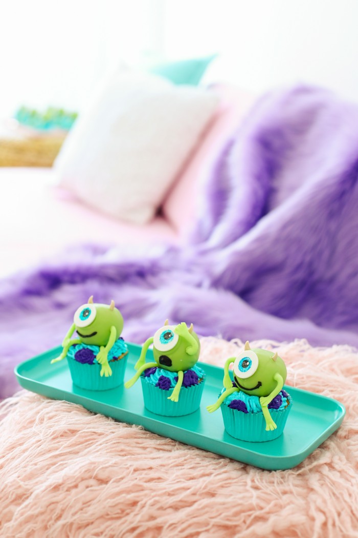 Mike wazowski Monsters Inc cupcakes sitting on a teal tray on a pink faux fur blanket