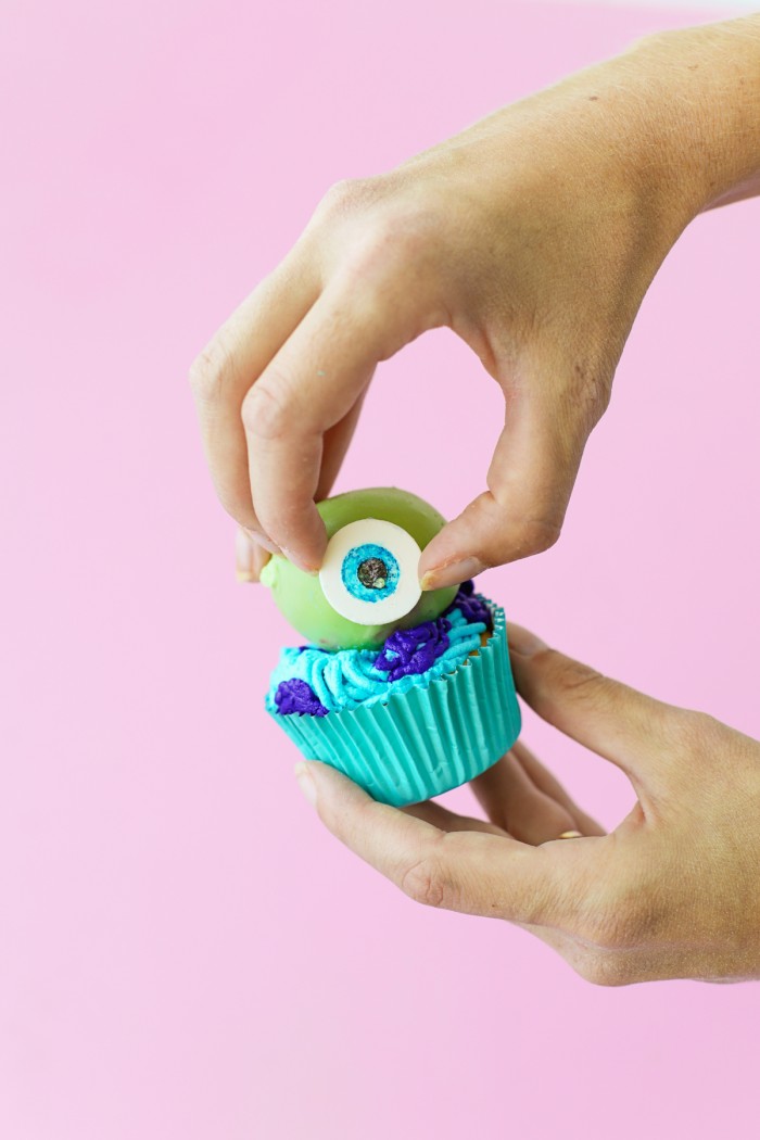 Fondant eye being placed on green cake ball on a cucpake