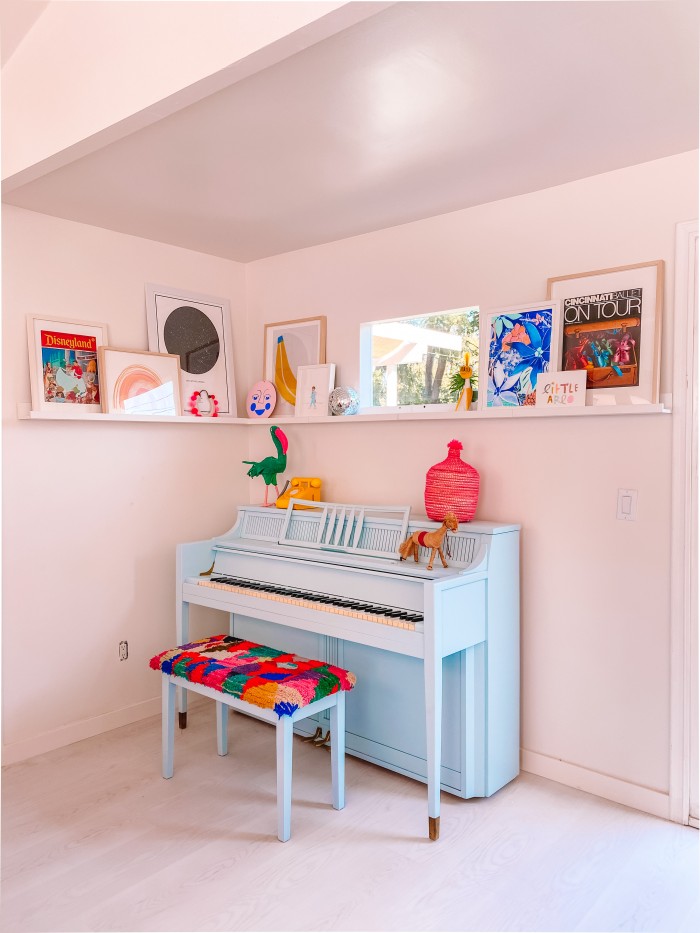 Blue piano in a corner with art on a ledge above and a window