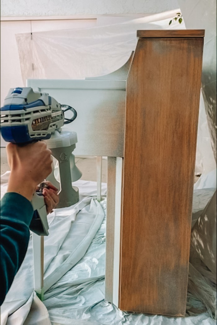 Painting the side of a wood piano with a paint sprayer