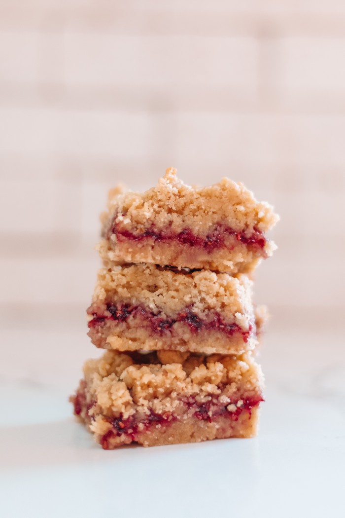 Three raspberry bars stacked in front of white tile