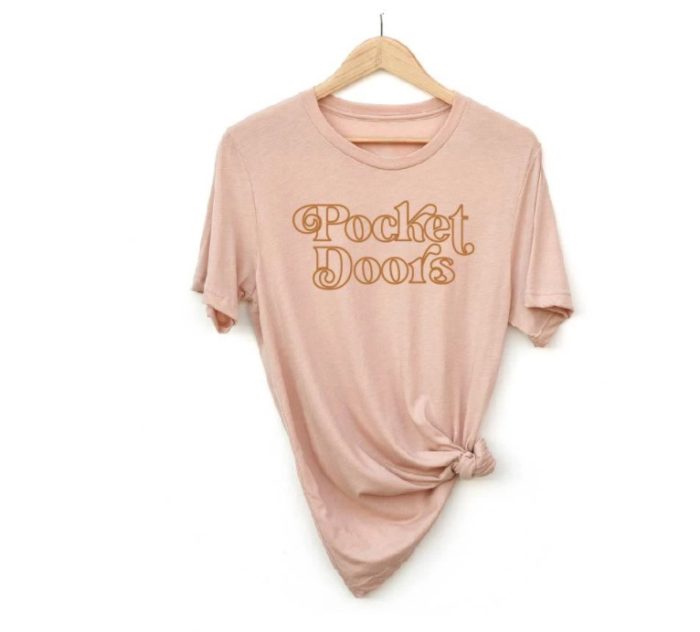 Pink shirt with yellow/gold writing "Pocket Doors" 