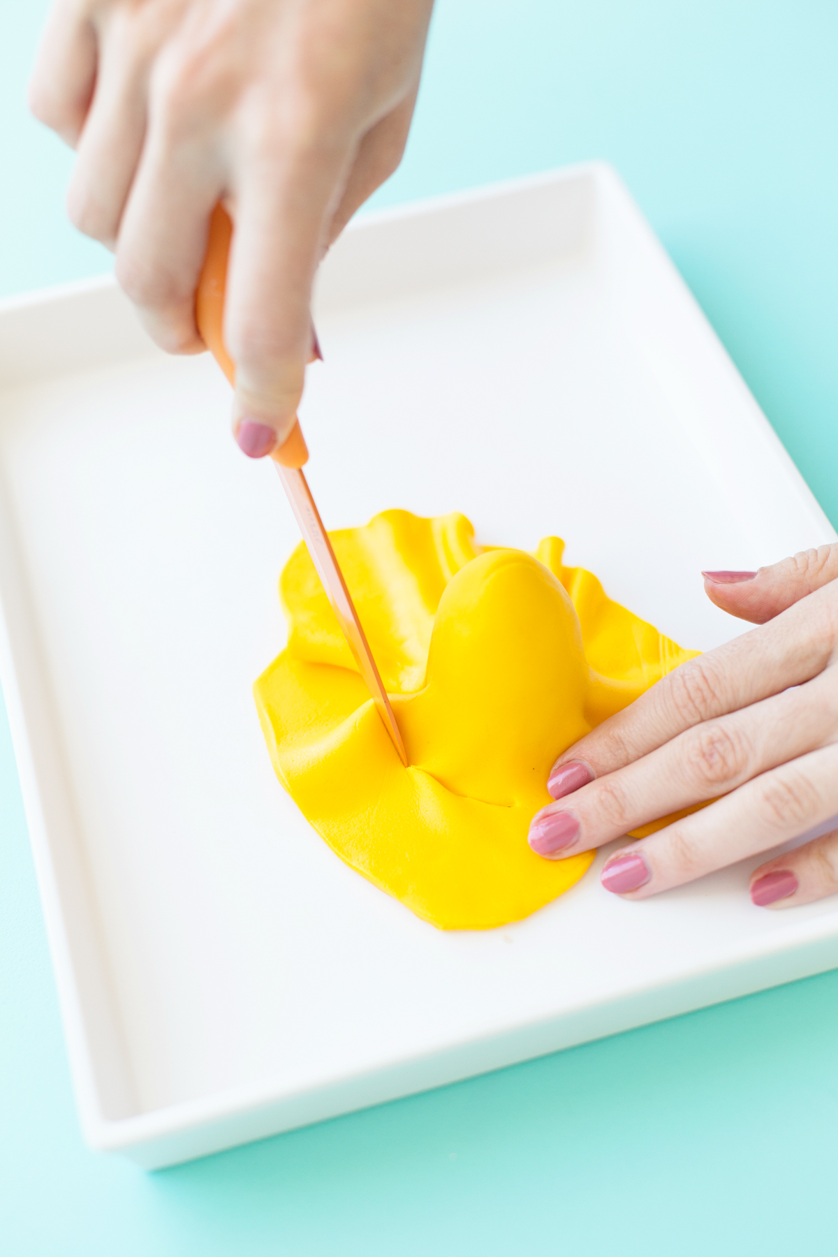 Yellow fondant draped on cake pop with knife cutting it